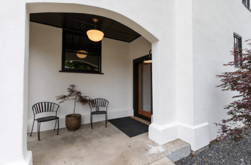 A minimalist entryway with two chairs, a potted plant, and a welcoming door under a covered porch.